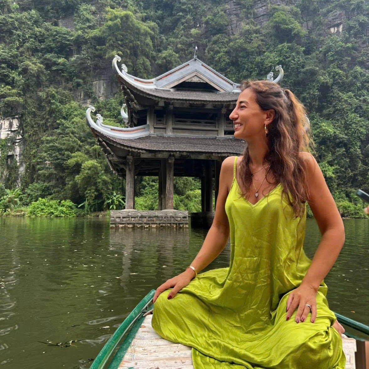 Una donna con un vestito giallo seduta a prua di una barca, davanti a un padiglione in riva al lago
