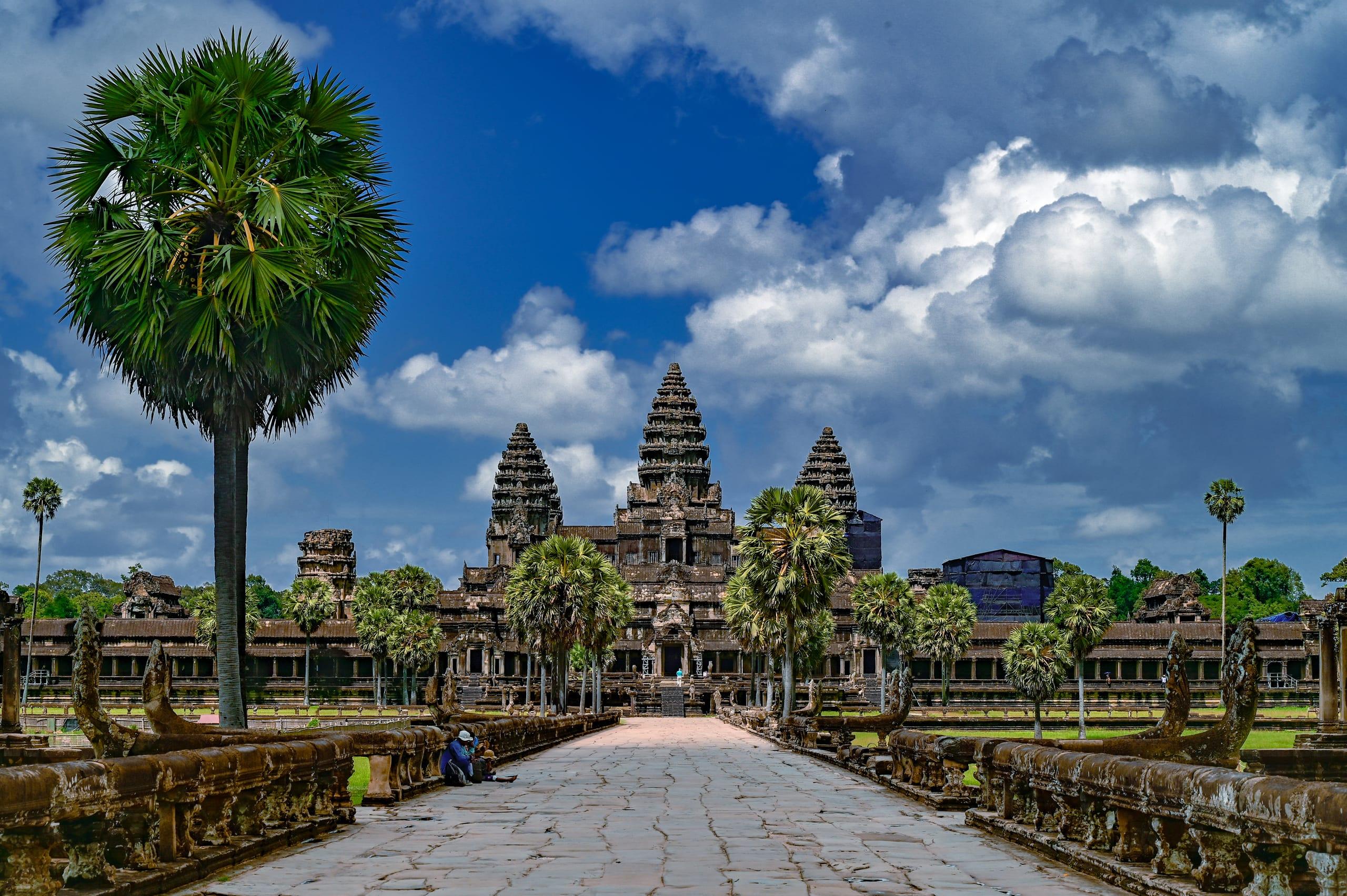 La strada rialzata che conduce alle torri di Angkor Wat, sotto un cielo azzurro con le palme