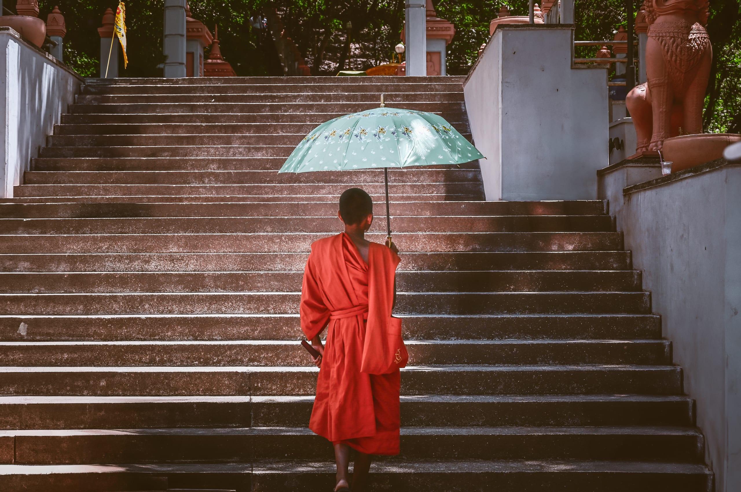 Un monaco con la veste arancione sale la scalinata di un tempio con un ombrello