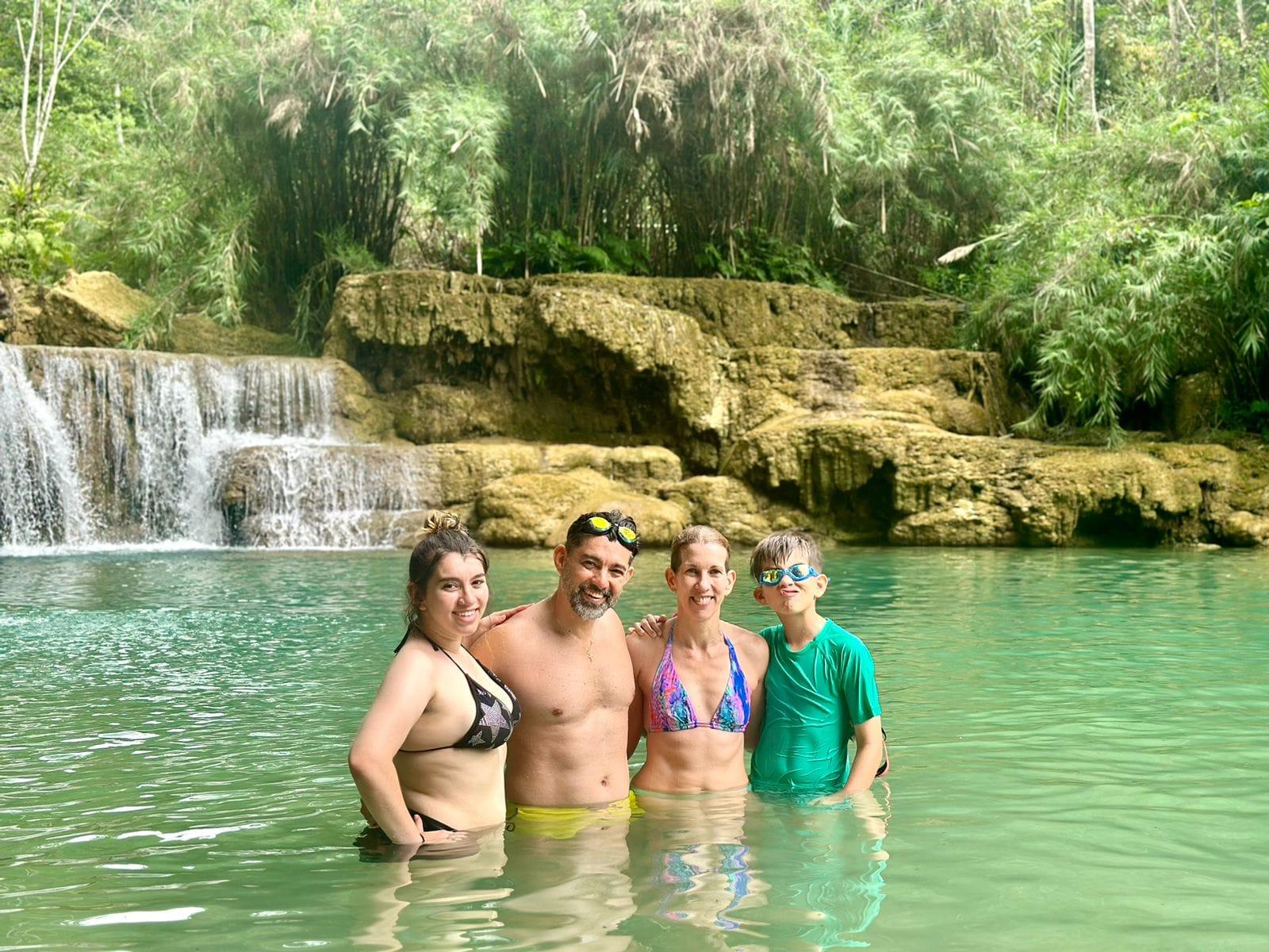 Una famiglia di quattro persone in piedi nella piscina naturale turchese ai piedi di una cascata a gradoni