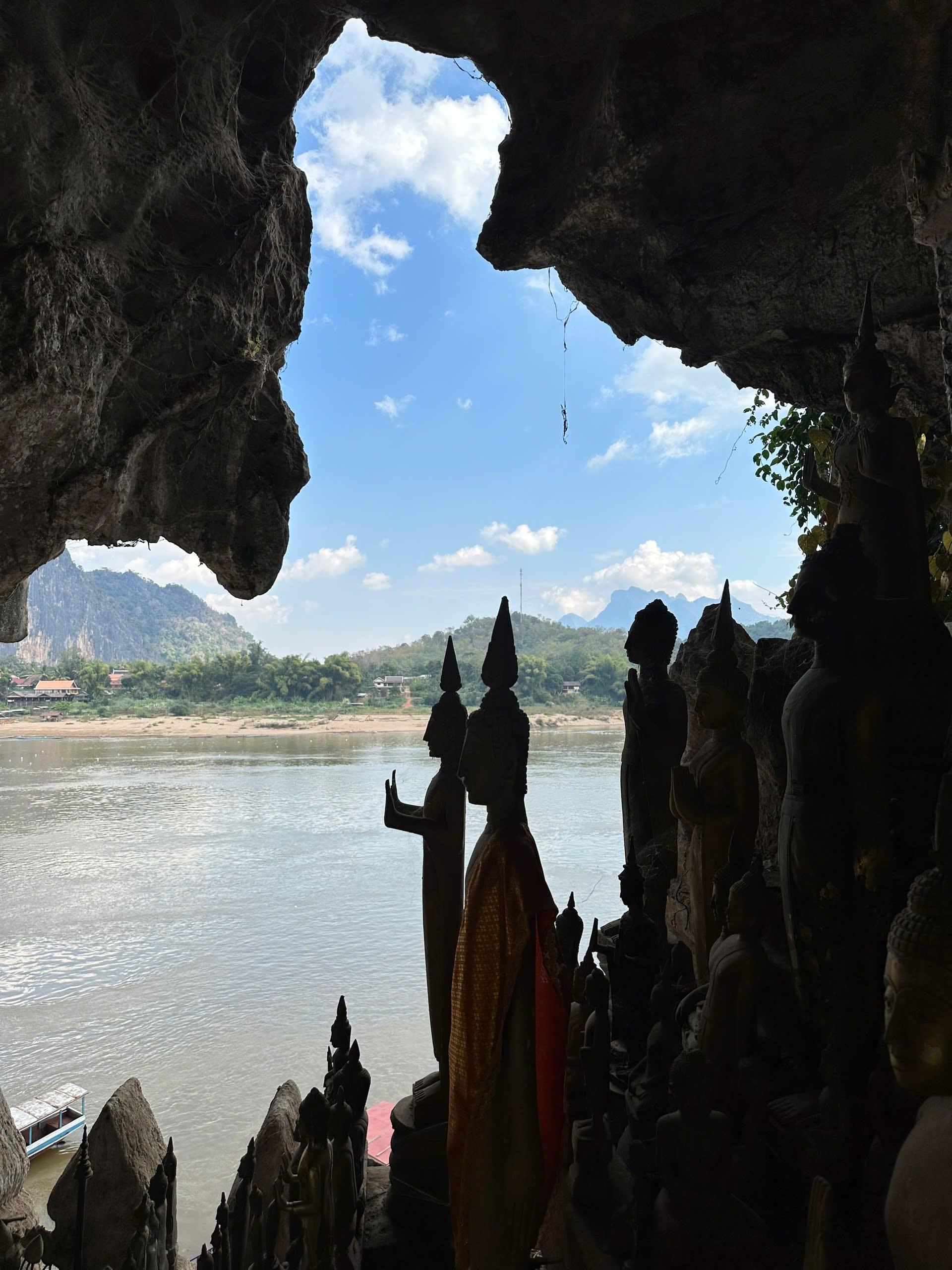 Statue del Buddha in controluce in una grotta sul fiume, rivolte verso l’acqua