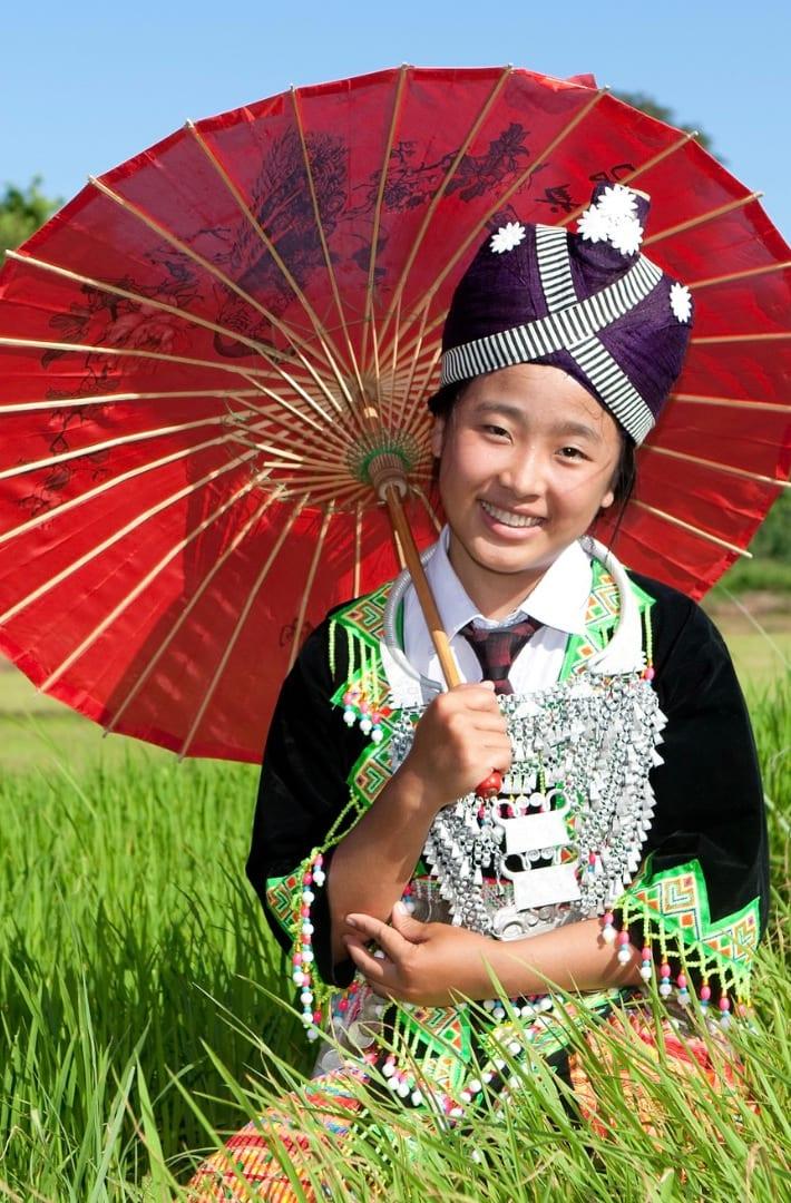 Una giovane donna in abito hmong regge un parasole rosso di carta in una risaia verde