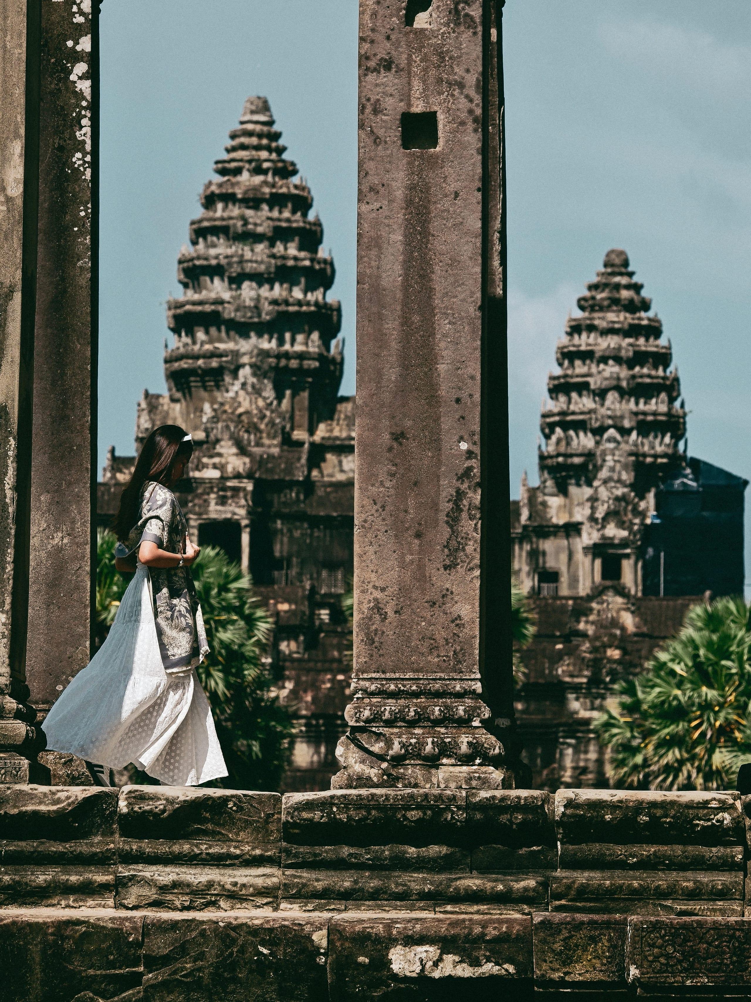 Una donna cammina tra colonne di pietra, con le torri di Angkor Wat alle spalle