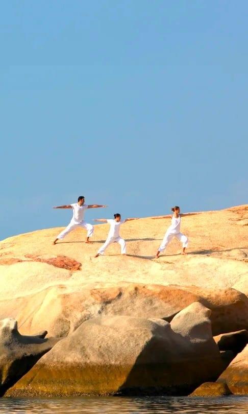Tre persone vestite di bianco praticano yoga su rocce di granito sopra il mare