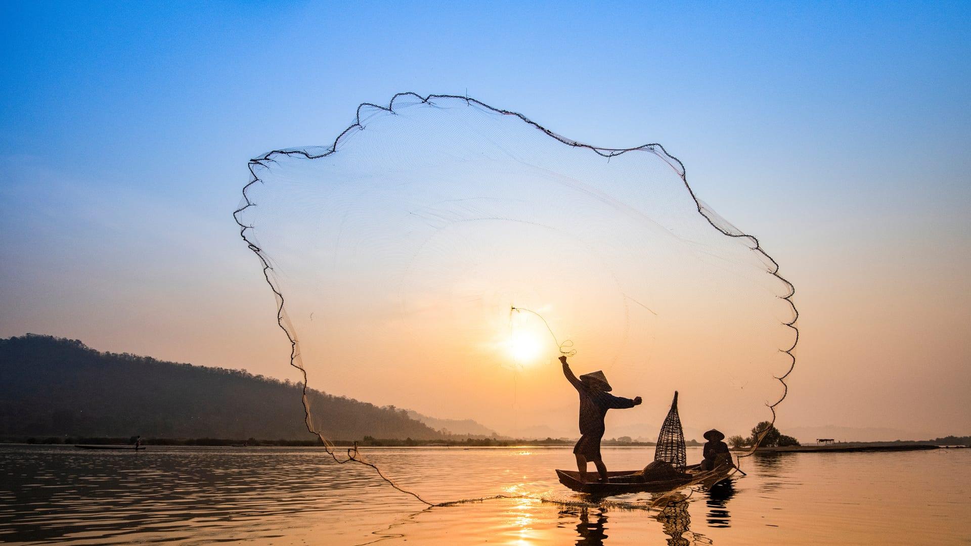 Un pescatore lancia la rete da una barca al tramonto