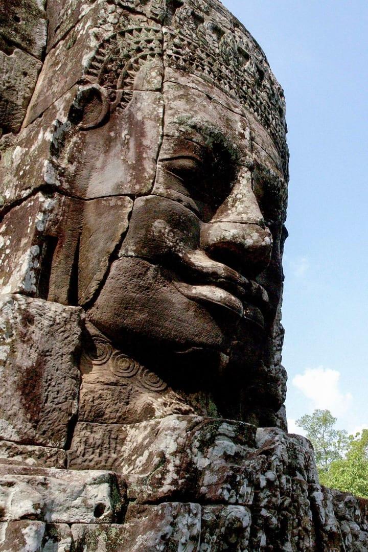 Un gigantesco volto di pietra scolpito sulla torre di un tempio, visto da vicino contro il cielo azzurro