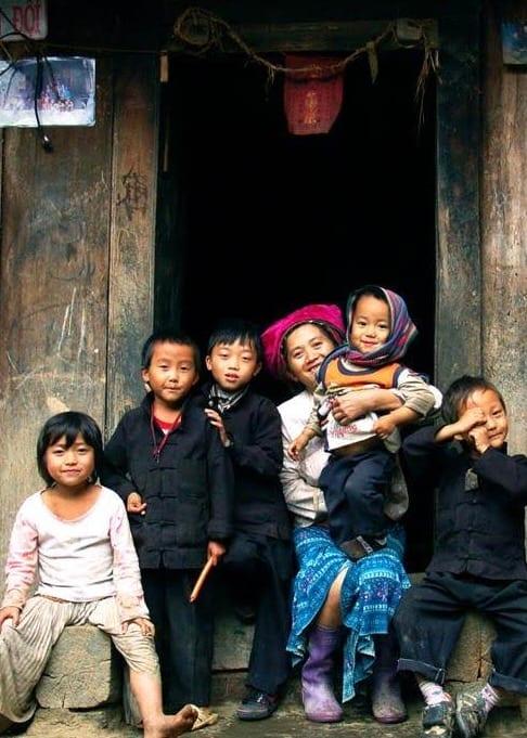 Bambini e una donna in abito tradizionale seduti insieme sulla soglia di una porta di legno