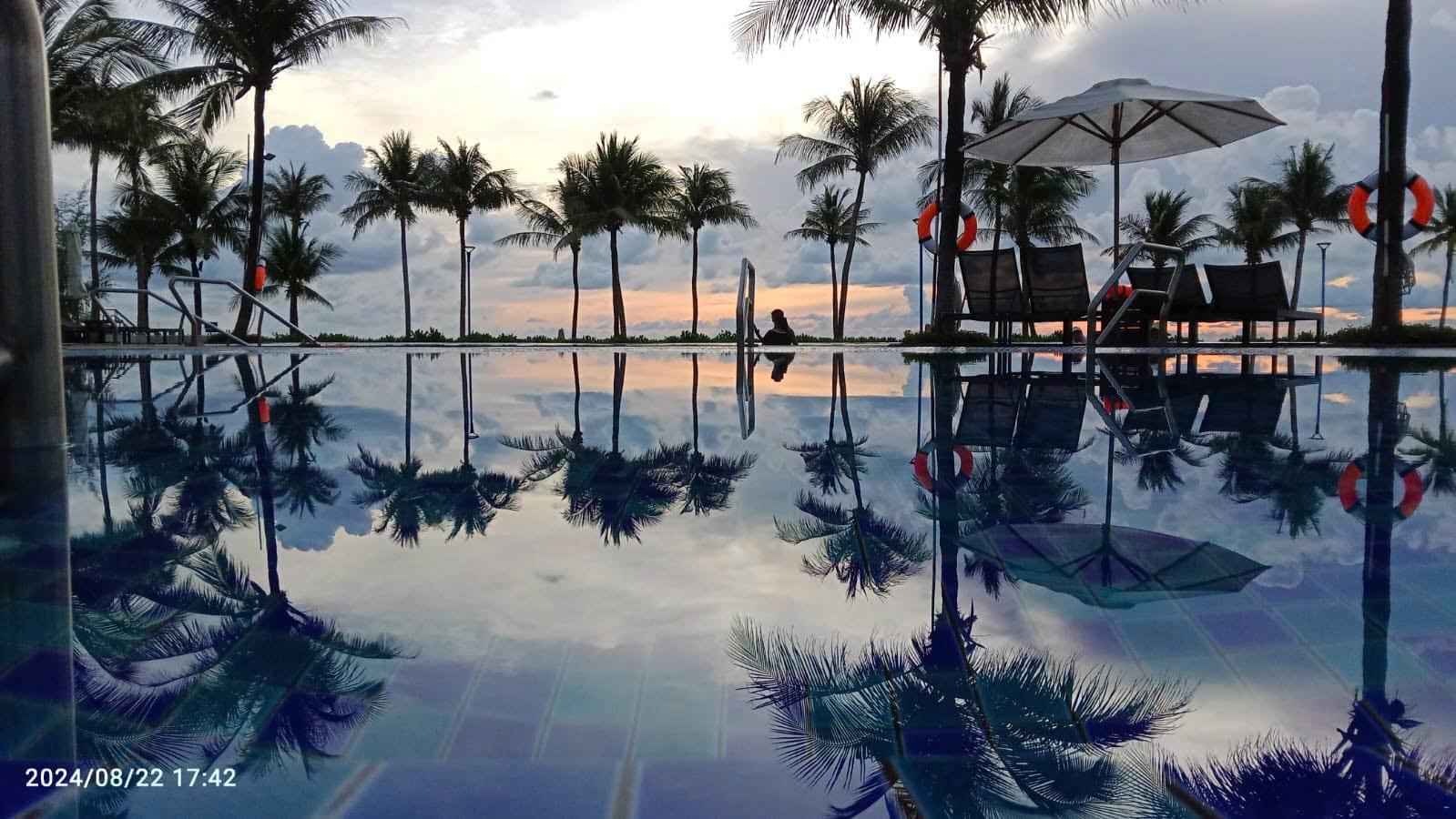 Palme e lettini riflessi nell’acqua immobile di una piscina al crepuscolo