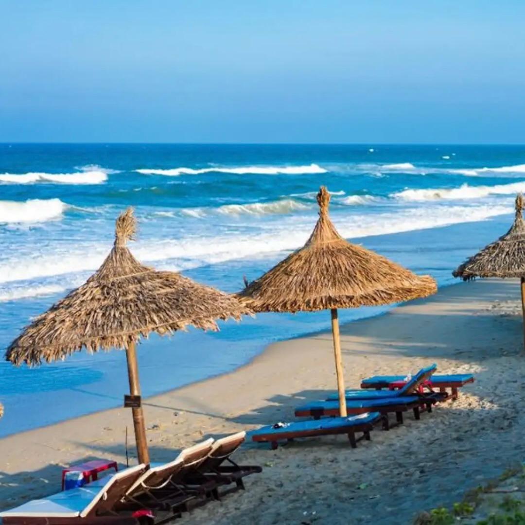 Ombrelloni di paglia e lettini su una spiaggia di sabbia, accanto alle onde che si infrangono