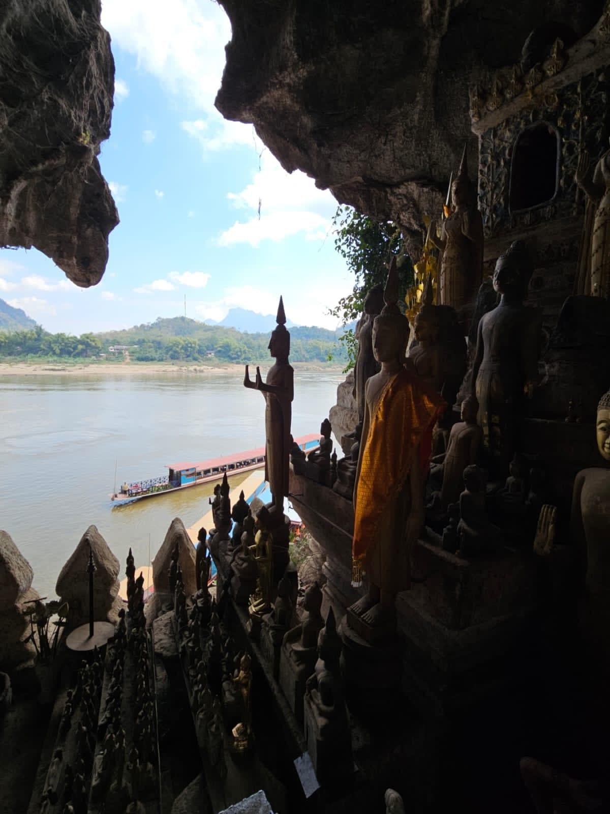 Statue del Buddha in una grotta sul fiume, rivolte verso l’acqua e le barche