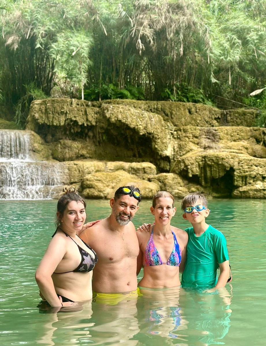 Una famiglia di quattro persone in piedi nella piscina naturale turchese ai piedi di una cascata a gradoni